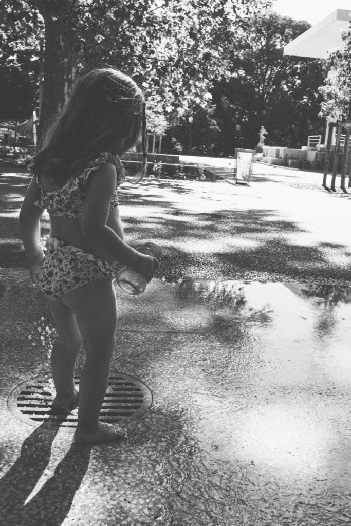 Une petite fille joue dans une flaque au soleil, en noir et blanc