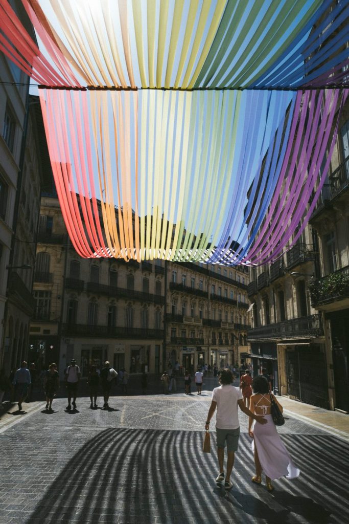 Une rue de Montpellier sous un plafond de rubans multicolores, des passants en contrebas