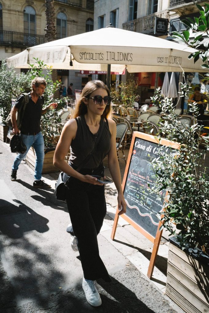 Une passante en lunettes de soleil devant une terrasse de café