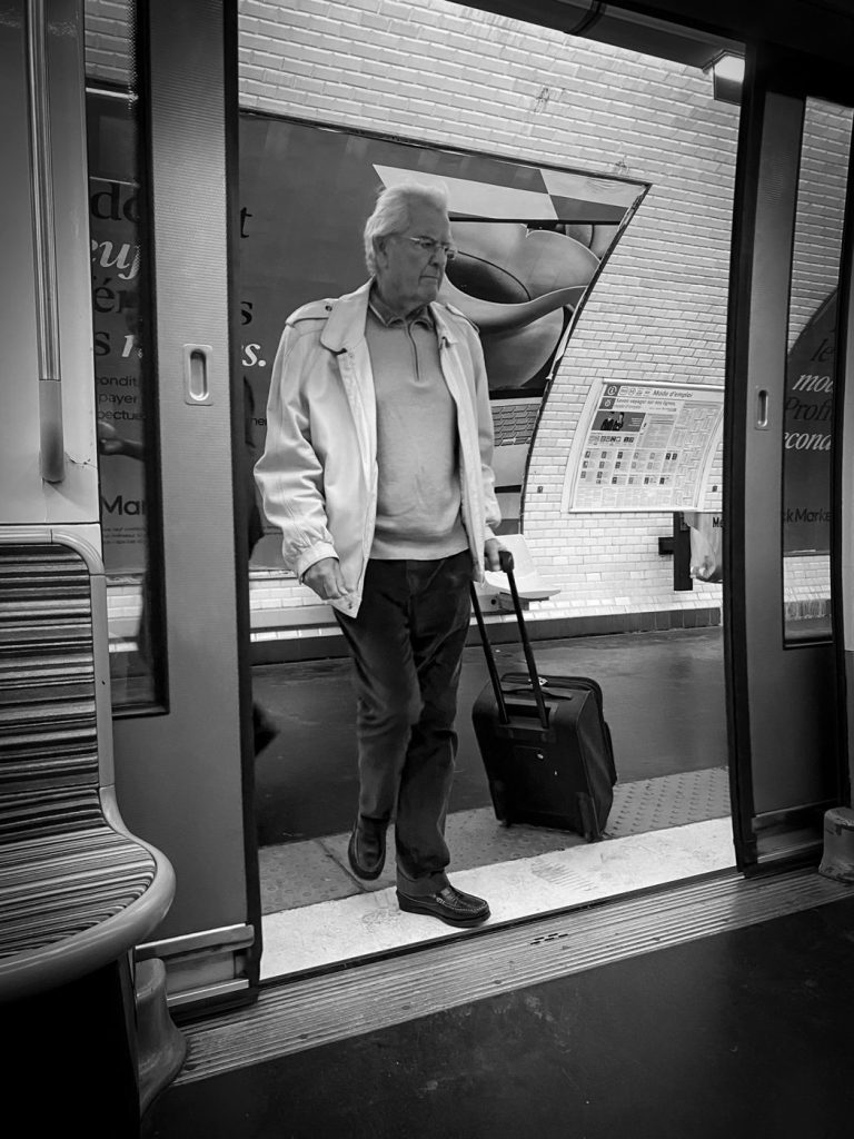 Un homme âgé descend d'un train avec sa valise, en noir et blanc