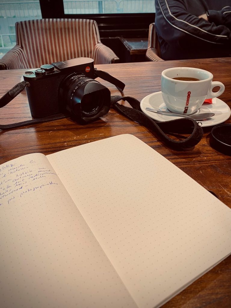 Un appareil photo, un carnet ouvert et un café sur une table de brasserie
