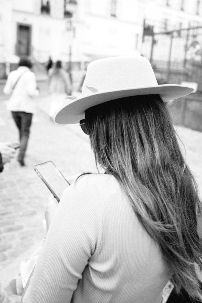 Une femme au chapeau de dos dans une rue pavée, en noir et blanc